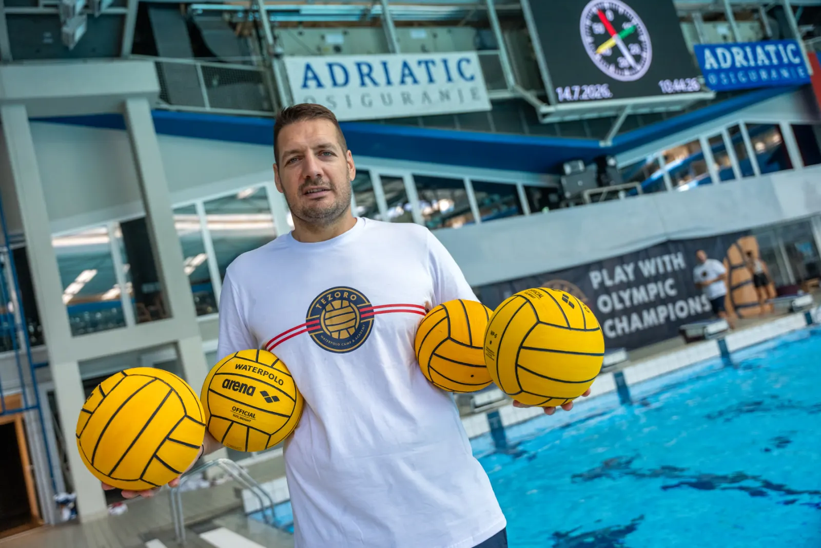 Coach holding four water polo balls on the pool deck